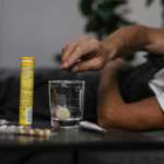 Eine Person liegt im Bett und schmeisst sich eine Brausetablette in ein Glas Wasser.